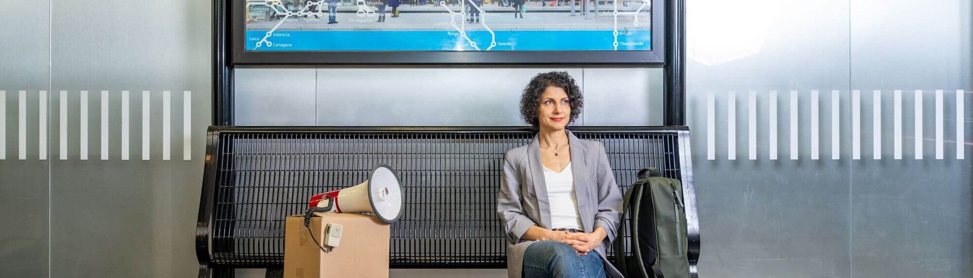 Mahnam Saeednia sits on a bench at the train station. Next to her is a package that points a megaphone at her.