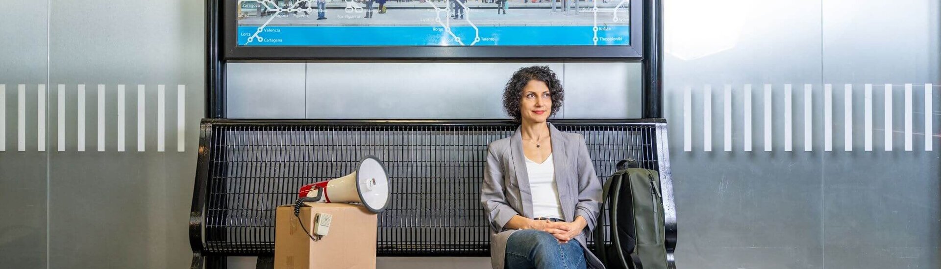 Mahnam Saeednia sits on a bench at the train station. Next to her is a package that points a megaphone at her.