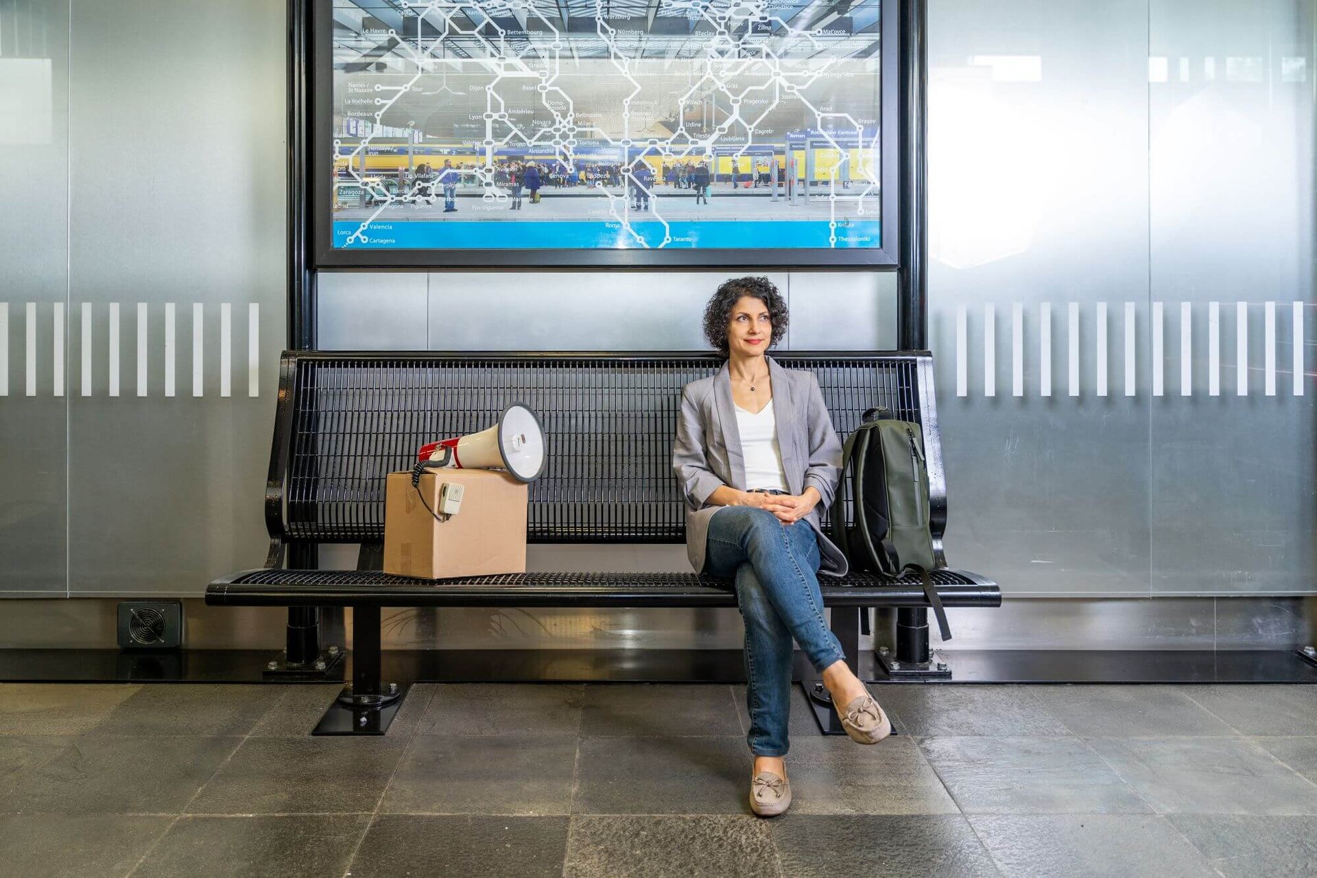 Mahnam Saeednia sits on a bench at the train station. Next to her is a package that points a megaphone at her.